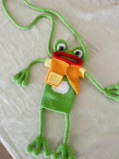 a green frog with a red hat and scarf on it's head is sitting on a white sheet