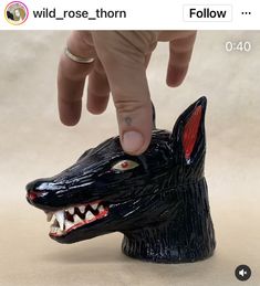 someone is touching the head of a black dog with red eyes and fangs on it's face