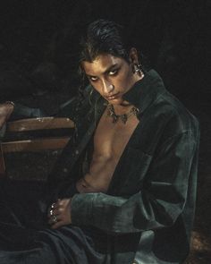 a shirtless man sitting on a wooden bench in the dark with his hands under his chest