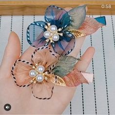 two handmade hair clips with flowers and pearls on top of each other in the palm of someone's hand