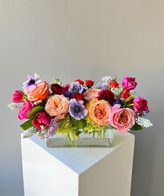 a vase filled with lots of colorful flowers on top of a white cubed table