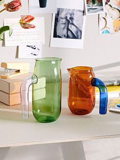 several different colored vases sitting on a table next to pictures and photos hanging on the wall