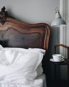 a bed with white linens and a wooden headboard next to a table with a cup on it