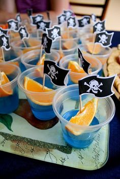 a table topped with cups filled with orange slices and pirate flags