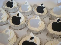 twelve cupcakes with white frosting and black apple on them in a box