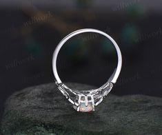 a white gold ring with an opal stone in the center on top of a rock