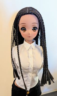 a doll with long braids wearing a white shirt and black pants, standing next to a wall