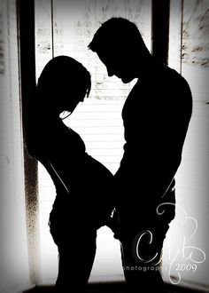 the silhouette of a man and woman standing next to each other in front of a window