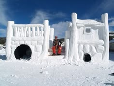 a man sitting in front of an ice sculpture on top of snow covered ground with buildings