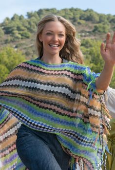 a woman is smiling and waving with her hand in the air while wearing a multicolored ponchy