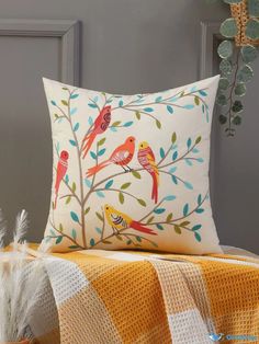 a decorative pillow with birds on it sitting next to a blanket and potted plant