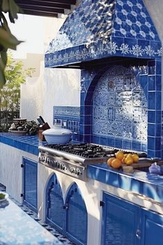 an outdoor kitchen with blue tiles on the walls and counter tops, along with oranges