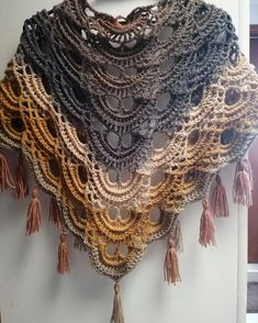 a crocheted shawl with tassels hanging from the side on a wall