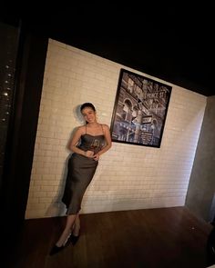 a woman standing in front of a white brick wall with a poster on the wall behind her