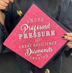 a woman holding up a pink graduation cap that says under profound pressure and great resilige diamonds are created