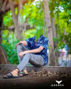 a young man sitting on the ground in front of trees