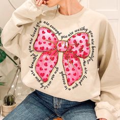 a woman sitting on a stool wearing a sweatshirt with a pink bow and words printed on it