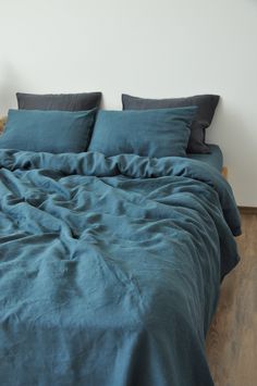 a bed with blue sheets and pillows on top of it in a room that has wood flooring