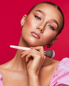 a woman is posing with her makeup brush in front of her face and wearing pink gingham