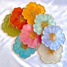 four different colored flowers sitting on top of a white cloth covered tablecloth with gold flecks