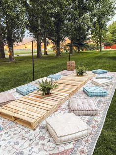 a wooden table with pillows and plants on it in the middle of a grassy area