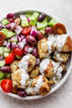 a white bowl filled with meatballs, tomatoes, cucumbers and other vegetables