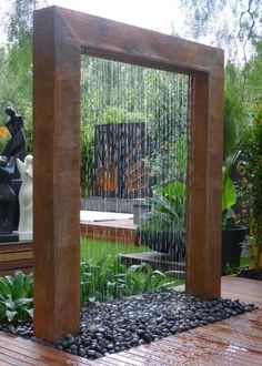 an outdoor fountain in the middle of a wooden deck with rocks and plants around it