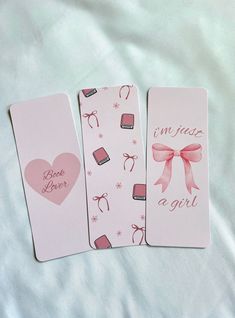 three bookmarks with pink bows on them sitting on a white bed sheet in the shape of hearts