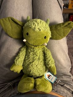 a green stuffed animal sitting on someone's lap