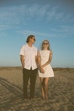 a man standing next to a woman on top of a sandy beach under a blue sky