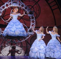 three women in blue dresses are on stage with their hands up and one woman is wearing a tiara