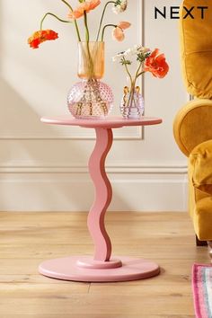 a pink table with vases and flowers on it in front of a yellow chair