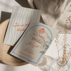 two wedding cards sitting on top of a wooden plate next to a vase with dried flowers