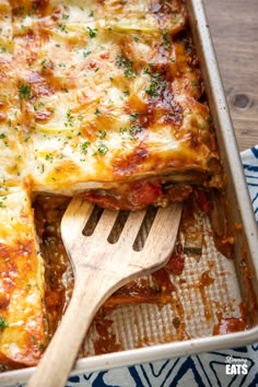 a casserole dish with meat, cheese and sauce on it next to a wooden spatula