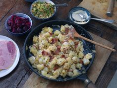 a pan filled with potatoes and meat next to other dishes on a wooden cutting board