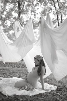 black and white photograph of a pregnant woman sitting on the ground in front of clothes