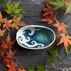 a blue and white bowl sitting on top of a wooden table next to autumn leaves