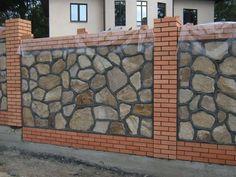 a brick wall with some rocks on the top and bottom part, behind it is a house