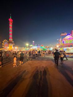 people are walking around an amusement park at night with carnival rides in the back ground