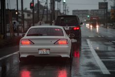 two cars are driving down the street in the rain at night, with red lights on