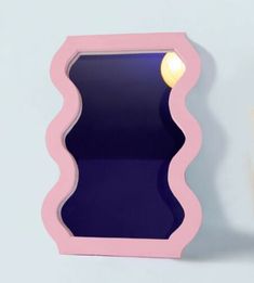 a pink and blue mirror with a light on it's side in front of a white wall