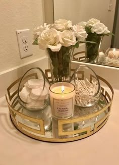 a candle sits on a tray with flowers and soaps in front of a mirror