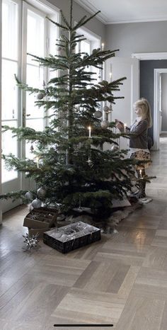 a woman is sitting on the floor next to a christmas tree with candles in it