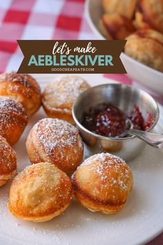 powdered sugar covered pastries on a white plate next to a bowl of jelly