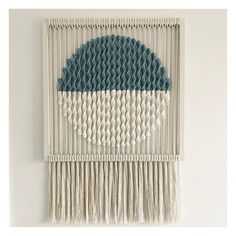 a wall hanging made out of yarn with a blue circle on the center and white fringes