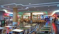 tables and chairs are lined up in the cafeteria area at an indoor mall with neon lights on the ceiling