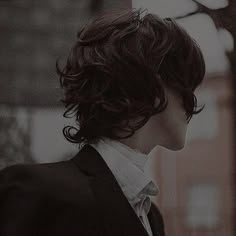 a young man with wavy hair wearing a suit and white shirt looking off into the distance