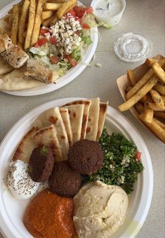 two plates filled with different types of food on top of a white tablecloth next to french fries