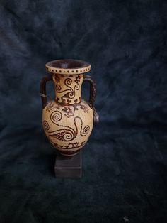 an old vase with designs on it sitting on a black surface in front of a dark background