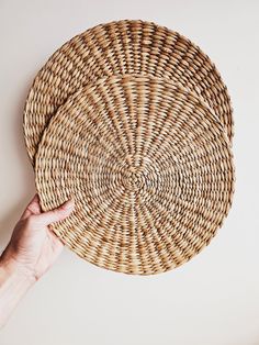 a hand holding a woven basket on top of a white wall